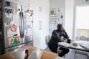 Mature African American man talking on cell phone and working at laptop at kitchen table