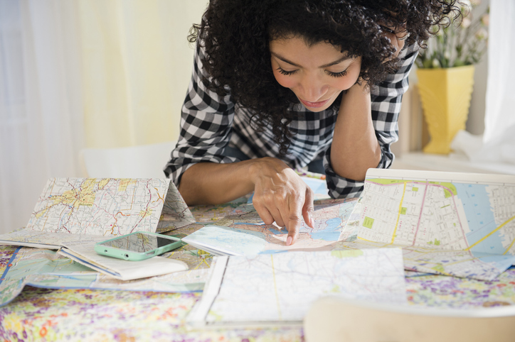Brunette woman points at a map on a table full of maps
