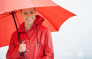A beautiful young woman standing outside while holding her red umbrella