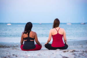 Photograph with rear view of two women meditating on beach, Newport, Rhode Island, USA