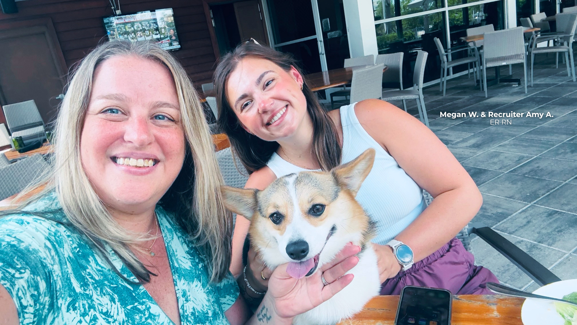 Two women sitting together outside with a corgie.