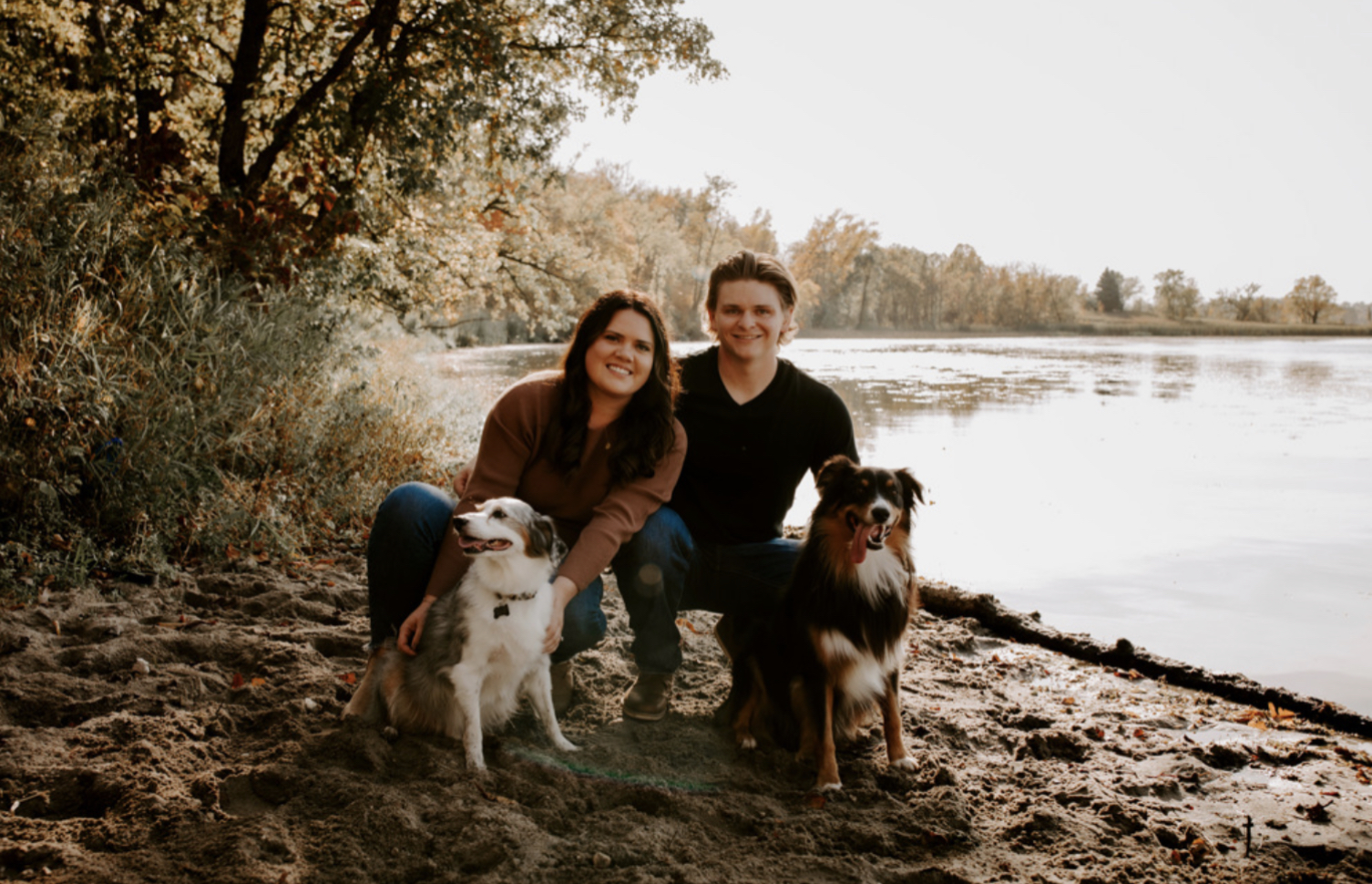 Man and woman sitting by a lake with their two dogs