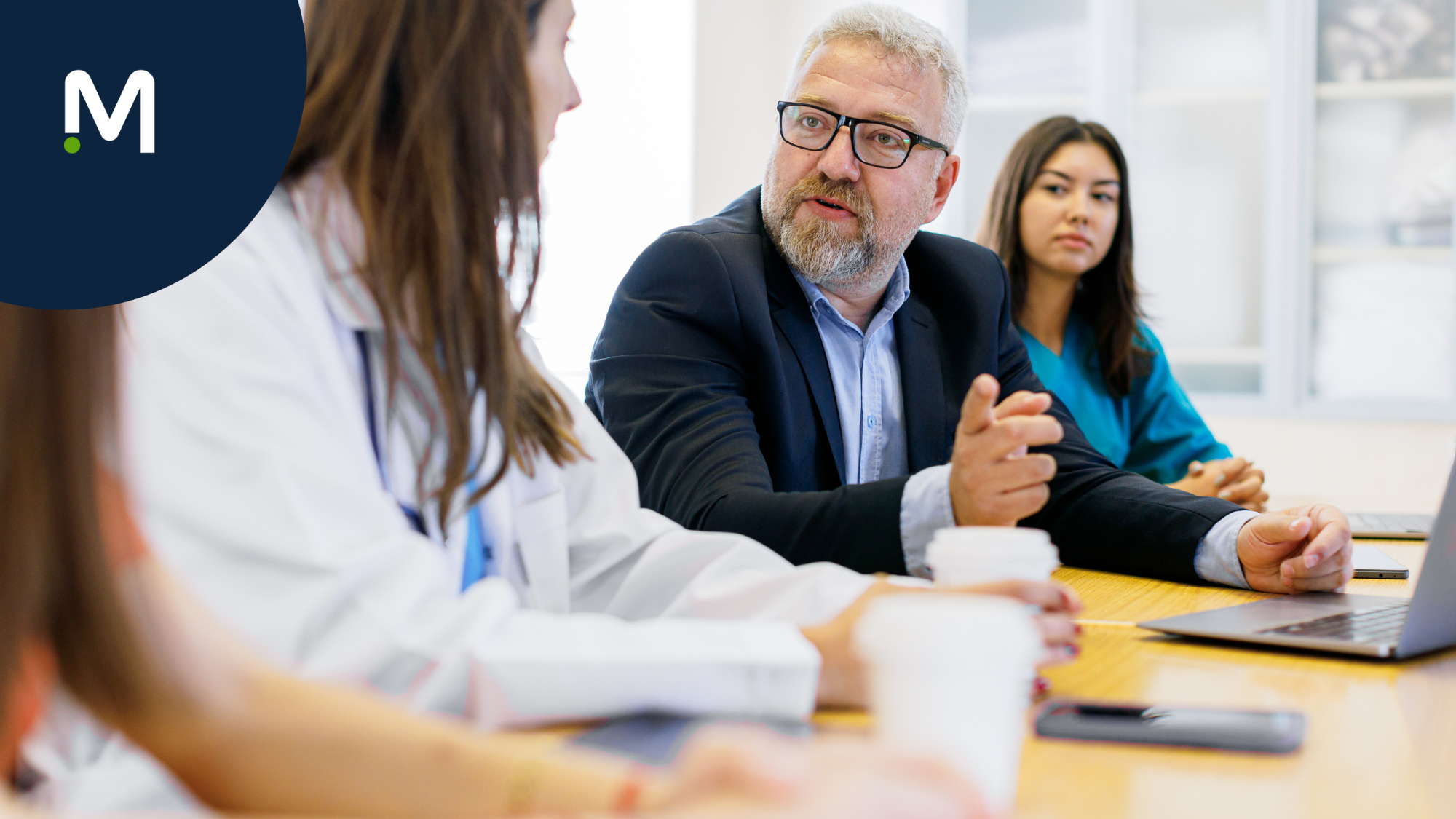 hospital-professionals-sitting-at-conference-table-medical-solutions-logo-in-corner