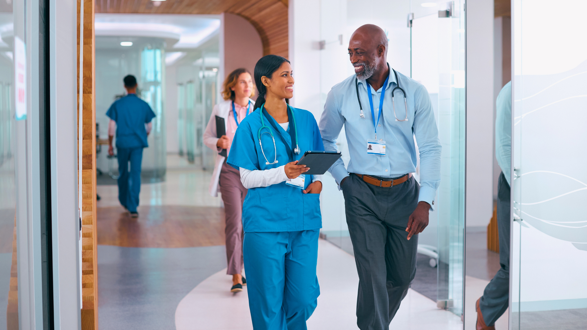 Male and female healthcare professional walking together down a hallway.