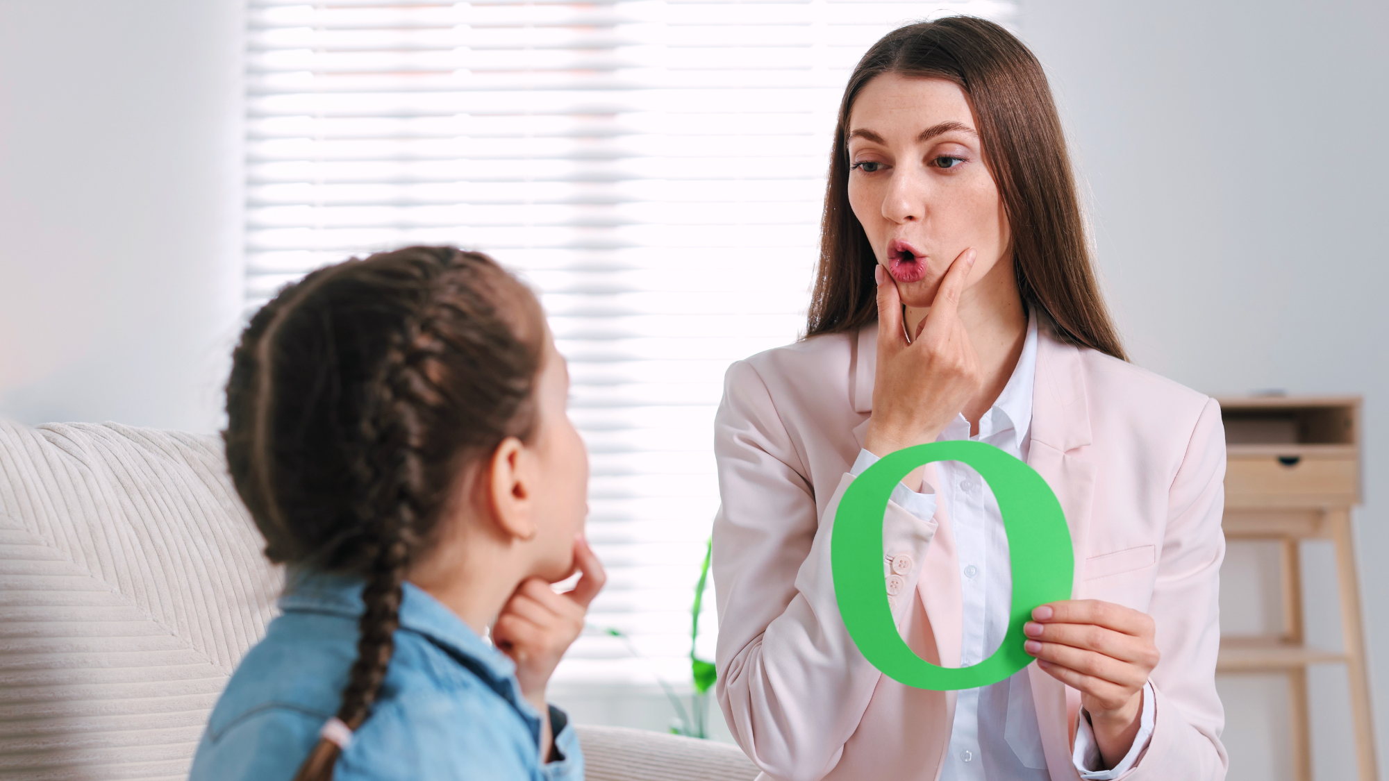 Female speech language pathologist holding an O and working with young girl.
