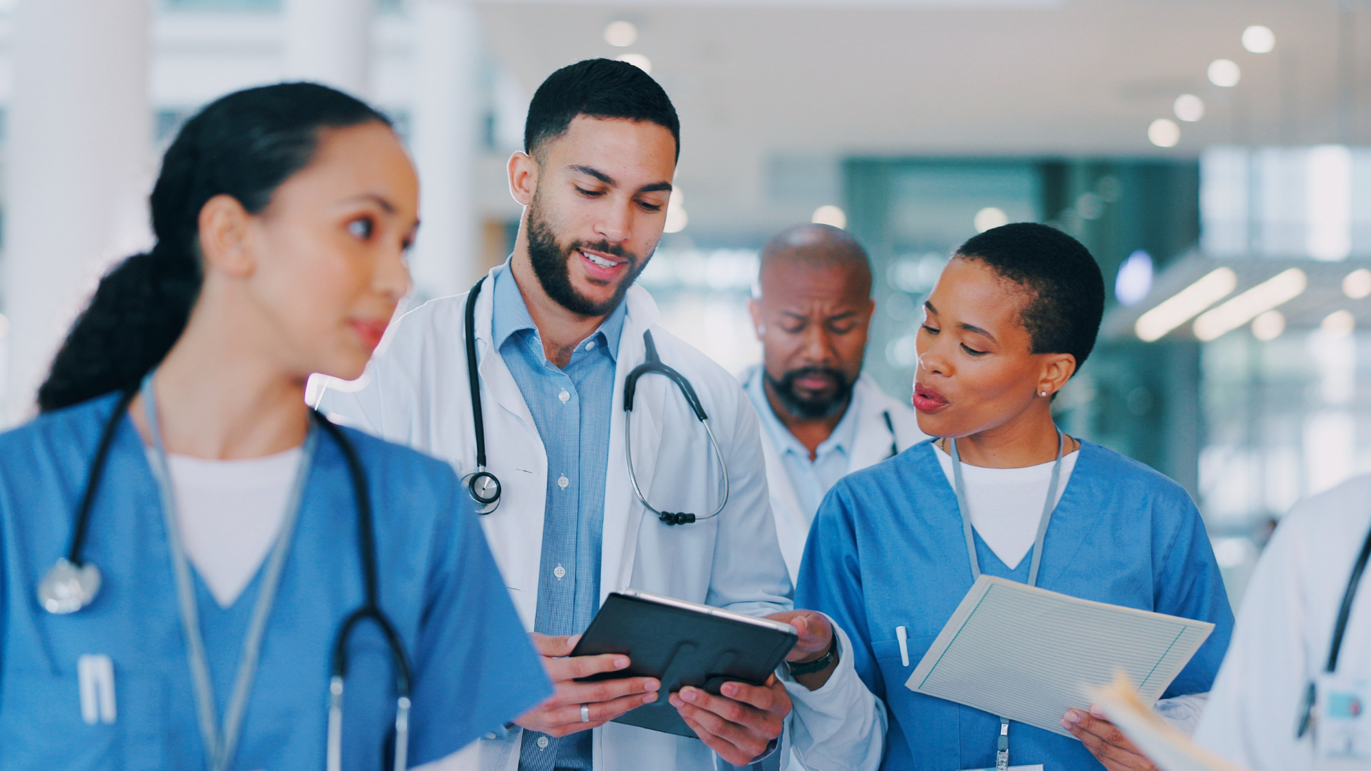 A male doctor showing a female nurse a tablet with another female nurse walking in front of them.