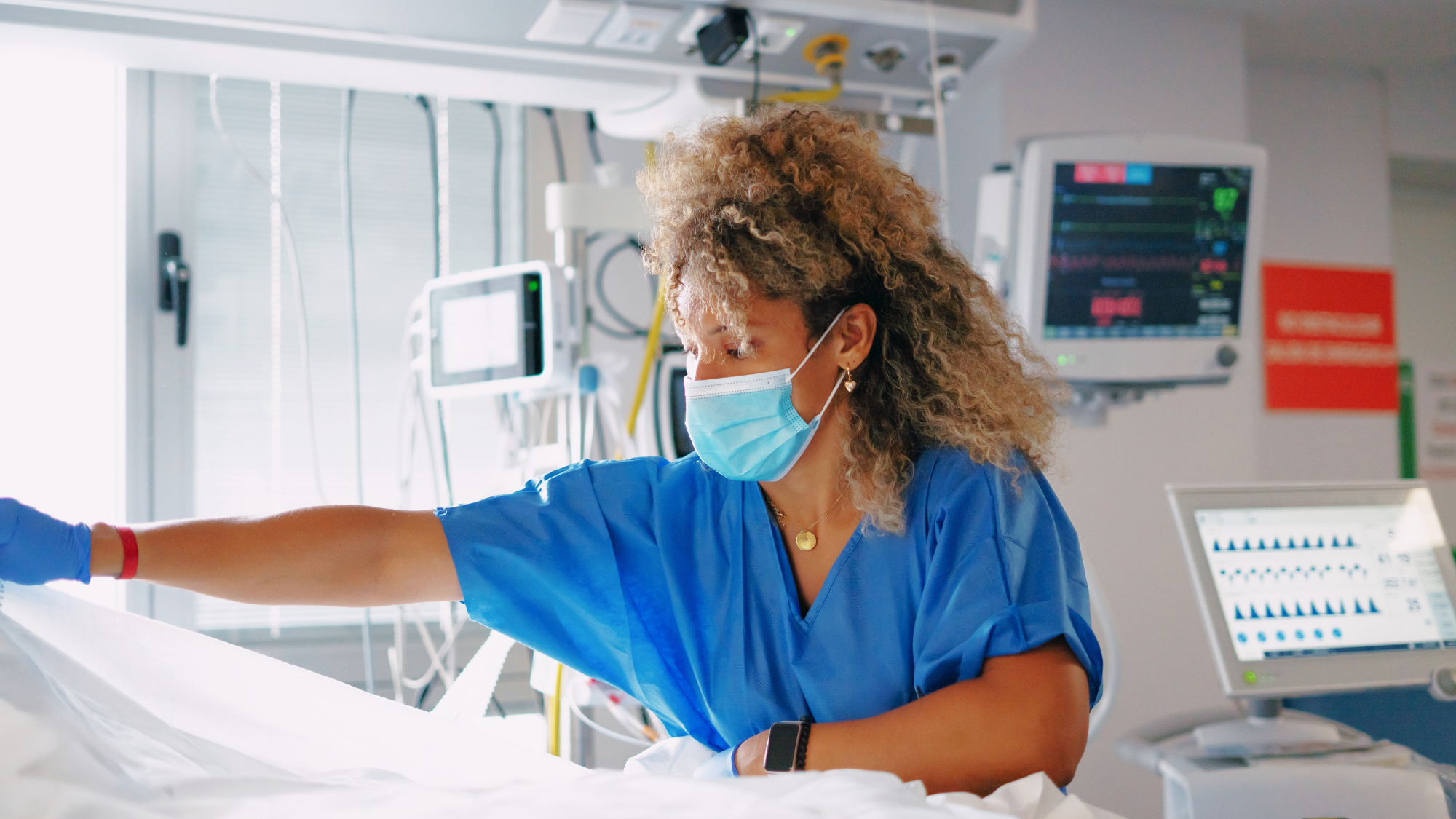 Female nurse wearing a mask working bedside.