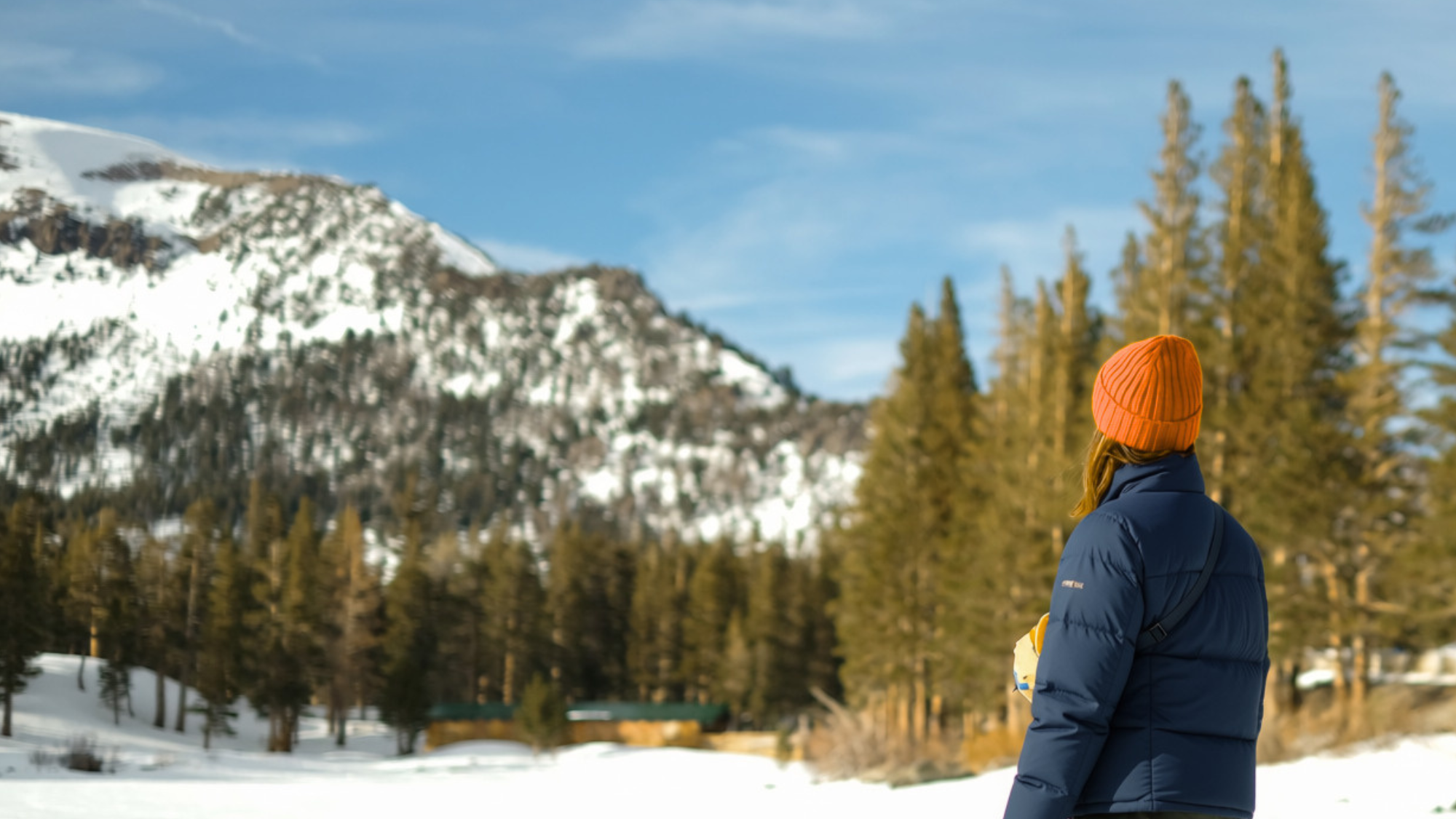 Woman in navy jacket and orange hat staring at the snowy mountains in Colorado.