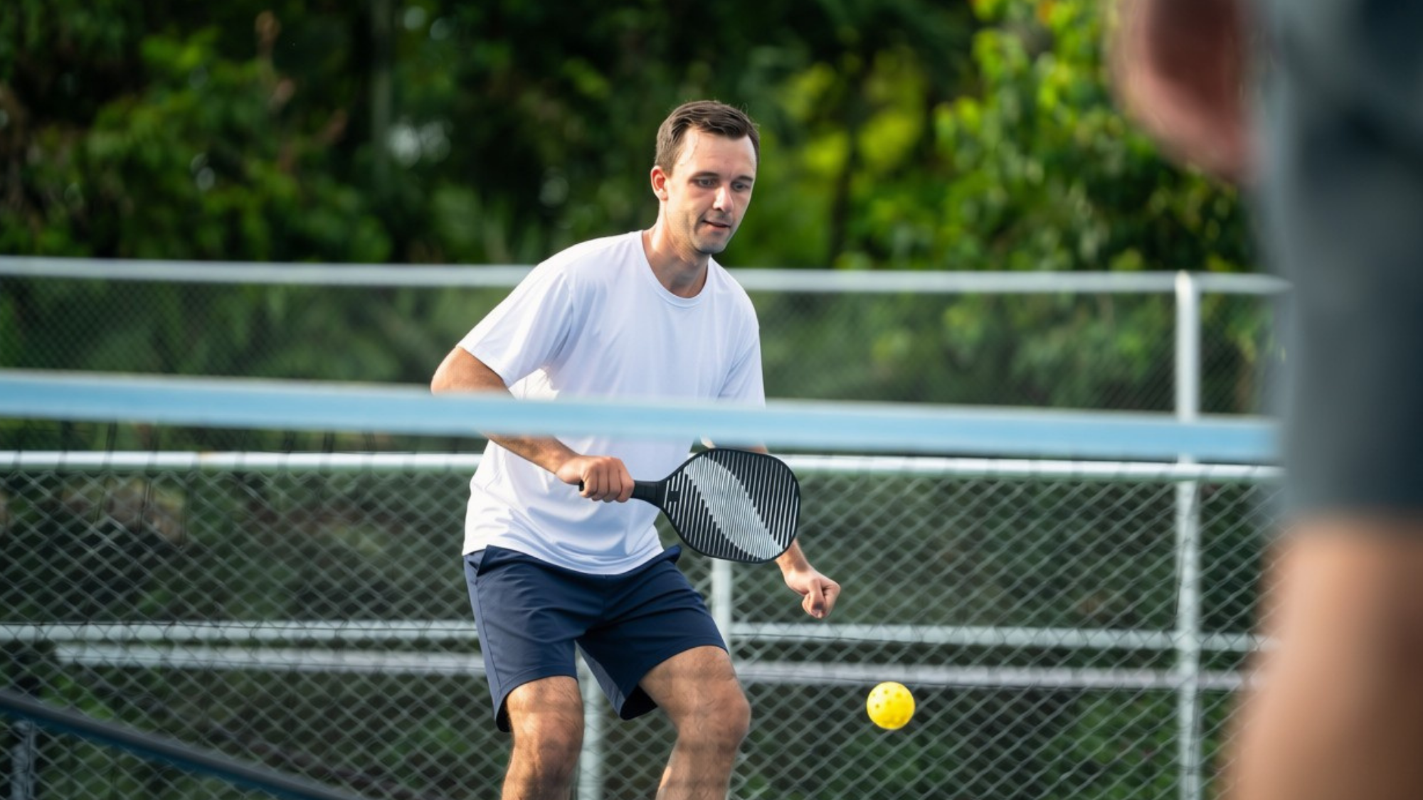 Man in white shirt and black shorts playing pickleball.