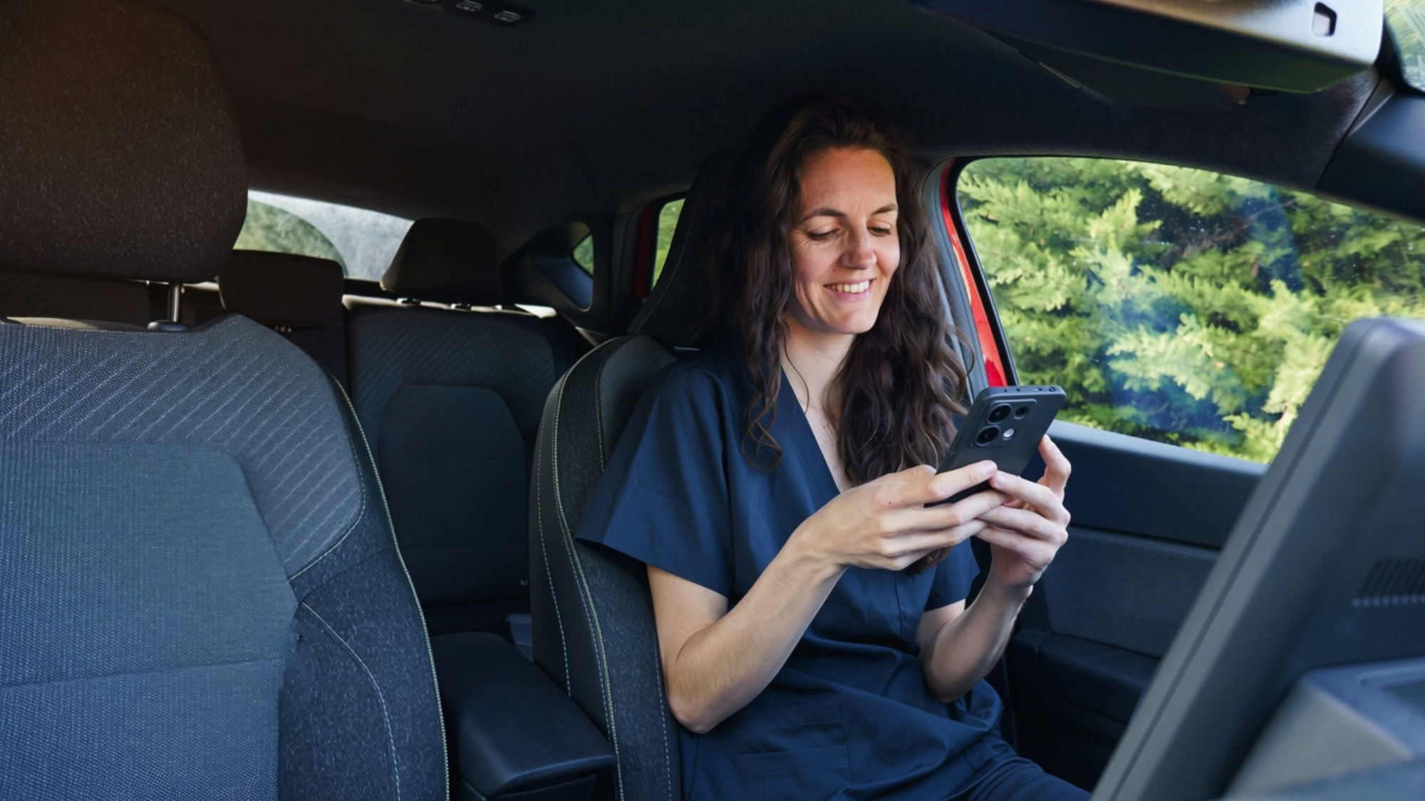 Female nurse looking at her phone while sitting in car.
