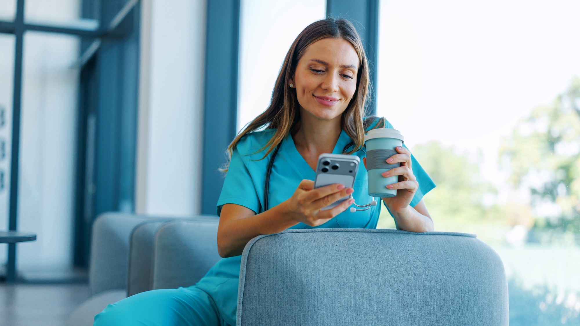 Female travel nurse looking at her phone drinking a coffee while on a break at a hospital.